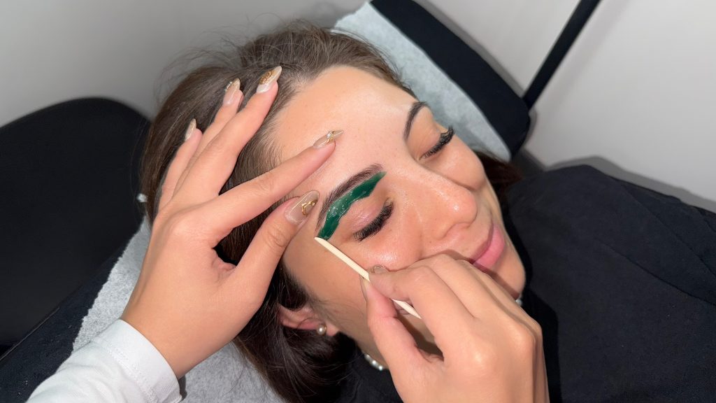 A brow artist at Lash Pilot Newport Beach is performing waxing for a client and they’re having a fun time.